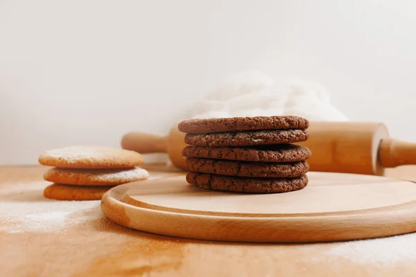 round cookies with sugar powder on a round wooden board, a basket of apples, a white towel on a light background surrounded by autumn leaves