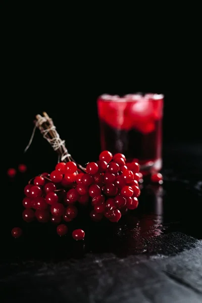 Vidro de inverno com um coquetel vermelho com gelo e uma palha, bagas vermelhas em um fundo preto molhado — Fotografia de Stock