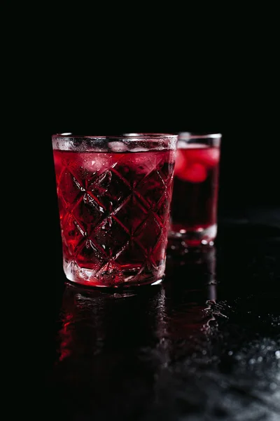 Dois copos com um coquetel vermelho com gelo em um fundo preto molhado — Fotografia de Stock