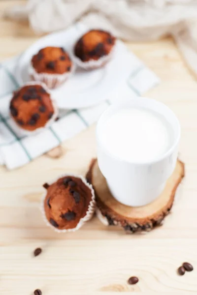 Cupcake al cioccolato, piattino bianco e tazza bianca con latte su un asciugamano verde su uno sfondo di legno chiaro — Foto Stock