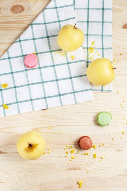 Elma ve hafif ahşap arka plan üzerinde kareli bir havlu üzerinde çok renkli macaroons