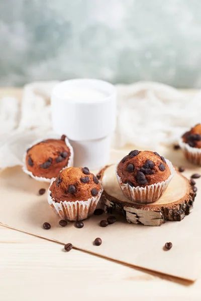 Cupcake al cioccolato, piattino bianco e tazza bianca con latte su un asciugamano verde su uno sfondo di legno chiaro — Foto Stock