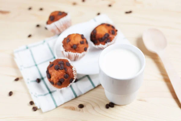 Cupcake al cioccolato, piattino bianco e tazza bianca con latte su un asciugamano verde su uno sfondo di legno chiaro — Foto Stock