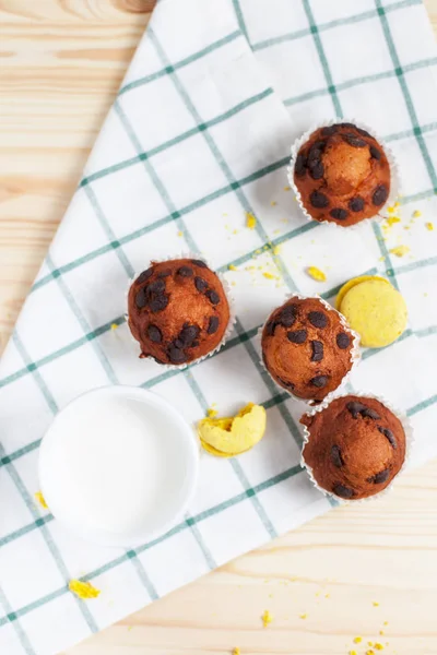 Cupcake al cioccolato, piattino bianco e tazza bianca con latte su un asciugamano verde su uno sfondo di legno chiaro — Foto Stock