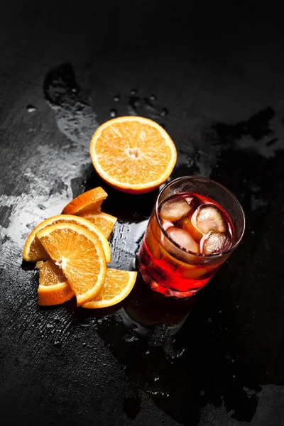 Um copo com um coquetel com gelo com laranja em um fundo escuro molhado — Fotografia de Stock