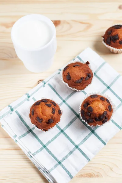 Cupcake al cioccolato, piattino bianco e tazza bianca con latte su un asciugamano verde su uno sfondo di legno chiaro — Foto Stock