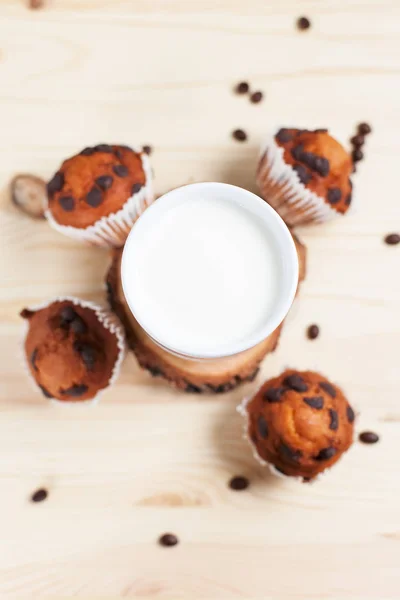 Cupcake al cioccolato, piattino bianco e tazza bianca con latte su un asciugamano verde su uno sfondo di legno chiaro — Foto Stock