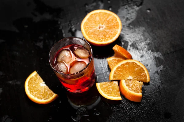 Una copa con un cóctel con hielo con naranja sobre un fondo húmedo y oscuro — Foto de Stock