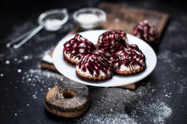 farklı içler berry tepesi ile serpilir, küçük tatlılar bir ahşap tahta üzerinde karanlık bir arka plan üzerinde beyaz bir tepside pudra şekeri serpilir