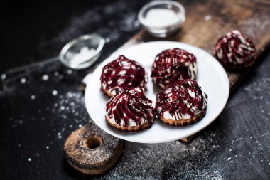 farklı içler berry tepesi ile serpilir, küçük tatlılar bir ahşap tahta üzerinde karanlık bir arka plan üzerinde beyaz bir tepside pudra şekeri serpilir