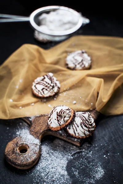 Petits gâteaux au chocolat avec différentes farces, saupoudrés de garniture au chocolat, saupoudrés de sucre en poudre sur une planche en bois, sur une serviette dorée sur un fond sombre — Photo
