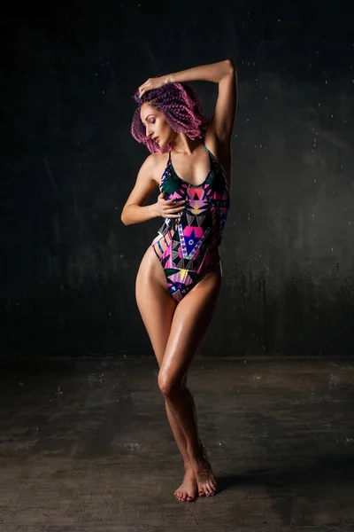 Young sexy girl with pink curly hair in a colored swimsuit on a black background, Water studio photo — Stock Photo, Image