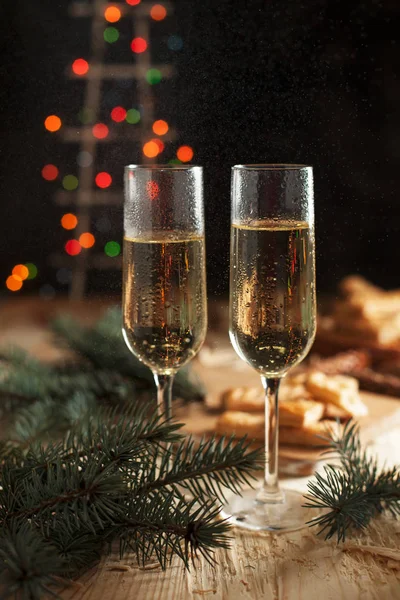 Occhiali con champagne, biscotti, un albero di Natale e le luci di anno nuovo sul tavolo festivo di un Anno nuovo — Foto Stock