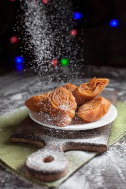 Beyaz tabakta yılbaşı masada şenlikli tatlılar yeşil peçete ve yılbaşı ışıkları karanlık bir arka plan üzerinde