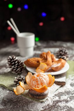 mandalina beyaz bir tabak, darbe ve bir fincan kakao, yeşil bir peçete ve yılbaşı ışıkları karanlık bir arka plan üzerinde bir yılbaşı masada