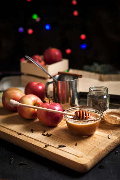 Приготовление выпеченных яблок к новогодним праздникам, рождественских елок и новогодних огней, меда и корицы на деревянной разделочной доске на темном фоне — стоковое фото