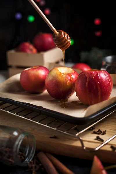 Приготовление выпеченных яблок к новогодним праздникам, рождественских елок и новогодних огней, меда и корицы на деревянной разделочной доске на темном фоне — стоковое фото
