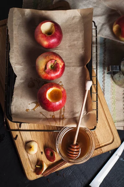 Cooking of baked apples for New Year's holidays, Christmas tree and New Year's lights, honey and cinnamon on a wooden cutting board on a dark background — Stock Photo, Image