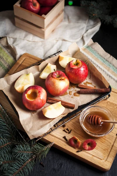 Yılbaşı tatil, yılbaşı ağacı ve yılbaşı ışıkları, bal ve tarçın karanlık bir arka plan üzerinde ahşap kesme tahtası için pişmiş elma yemek