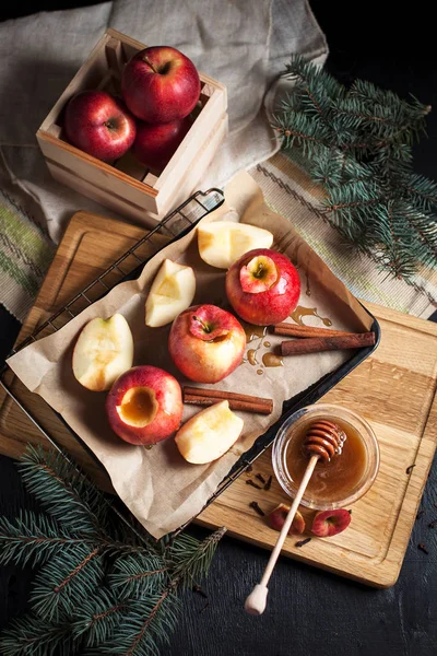 Yılbaşı tatil, yılbaşı ağacı ve yılbaşı ışıkları, bal ve tarçın karanlık bir arka plan üzerinde ahşap kesme tahtası için pişmiş elma yemek