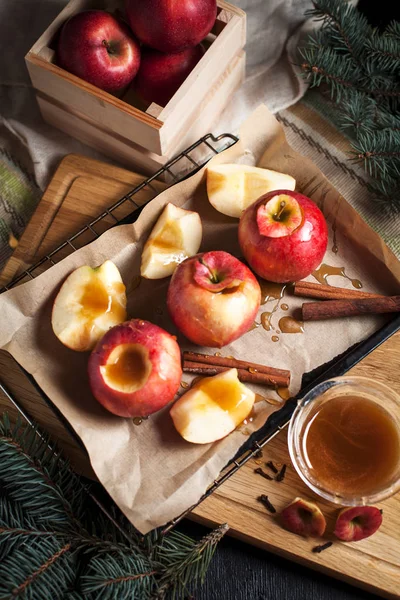 La cocción de las manzanas cocidas para las fiestas de Año Nuevo, el árbol de Navidad y las luces de Año Nuevo, la miel y la canela en una tabla de cortar de madera sobre un fondo oscuro — Foto de Stock