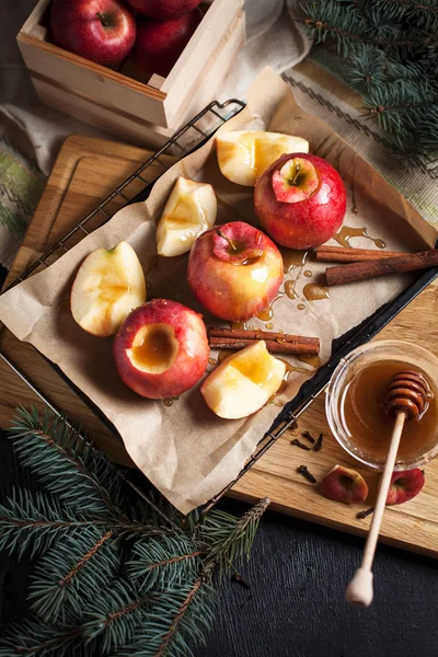 Yılbaşı tatil, yılbaşı ağacı ve yılbaşı ışıkları, bal ve tarçın karanlık bir arka plan üzerinde ahşap kesme tahtası için pişmiş elma yemek