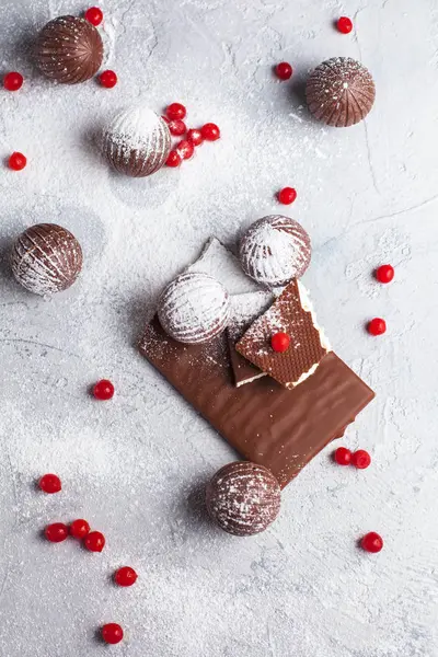 chocolate round candies, chocolate bars and red berries on a gray background and powdered sugar