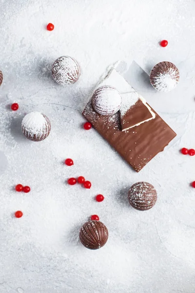 chocolate round candies, chocolate bars and red berries on a gray background and powdered sugar