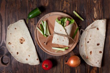 Yeşiller, salatalık, domates ve bir yuvarlak ahşap tahta ahşap arka plan üzerinde üzerinde sosis pişirme börek