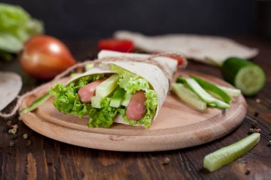  Yeşiller, salatalık, domates ve bir yuvarlak ahşap tahta ahşap arka plan üzerinde üzerinde sosis dürüm