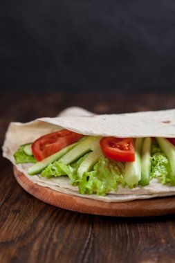  Yeşiller, salatalık, domates ve bir yuvarlak ahşap tahta ahşap arka plan üzerinde üzerinde sosis dürüm