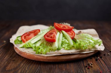  Yeşiller, salatalık, domates ve bir yuvarlak ahşap tahta ahşap arka plan üzerinde üzerinde sosis dürüm