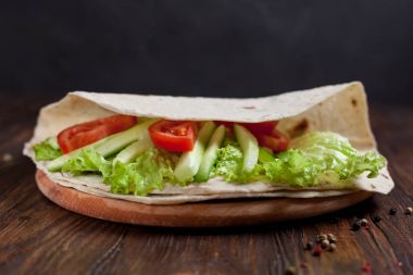  Yeşiller, salatalık, domates ve bir yuvarlak ahşap tahta ahşap arka plan üzerinde üzerinde sosis dürüm