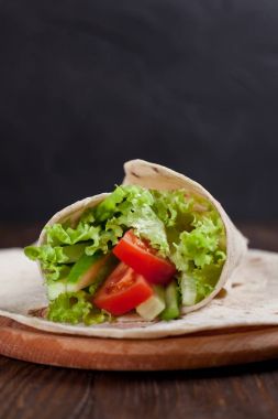  Yeşiller, salatalık, domates ve bir yuvarlak ahşap tahta ahşap arka plan üzerinde üzerinde sosis dürüm