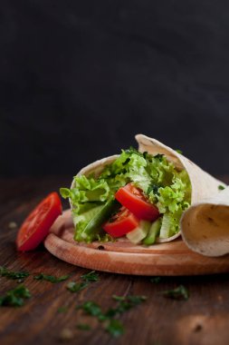  Yeşiller, salatalık, domates ve bir yuvarlak ahşap tahta ahşap arka plan üzerinde üzerinde sosis dürüm