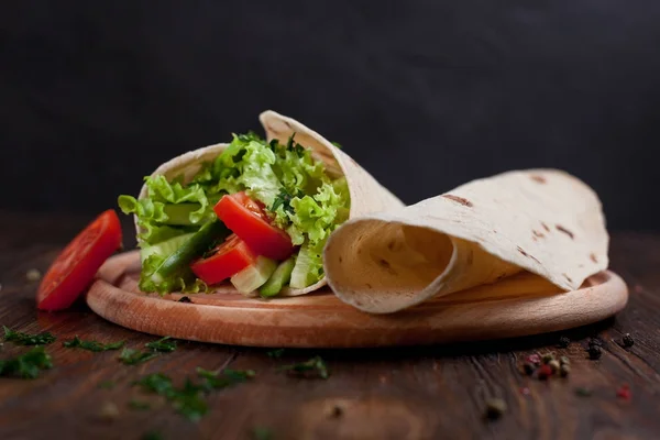 Burrito s zelení, okurky, rajčata a klobásy na kulaté dřevěné desce na dřevěné pozadí — Stock fotografie