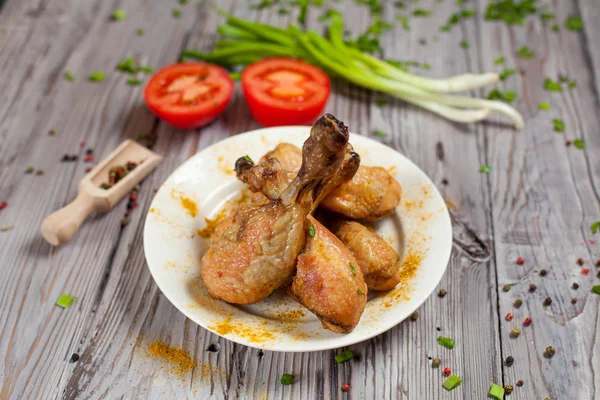 Im Ofen gebackene Hühnerkeulen mit grünen Zwiebeln und Tomaten auf einem Holzbrett auf hellem Holzgrund — Stockfoto