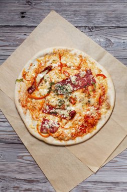 Peynir, pastırma, biber ve hafif ahşap arka plan üzerinde otlar ile ince hamur pizza