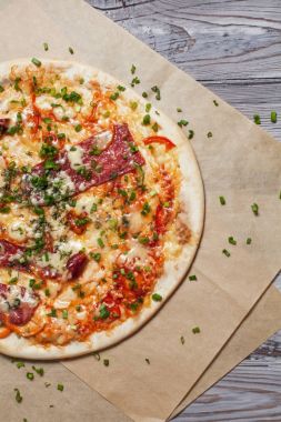 Peynir, pastırma, biber ve hafif ahşap arka plan üzerinde otlar ile ince hamur pizza