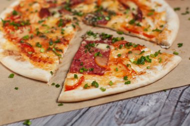 Peynir, pastırma, biber ve hafif ahşap arka plan üzerinde otlar ile ince hamur pizza