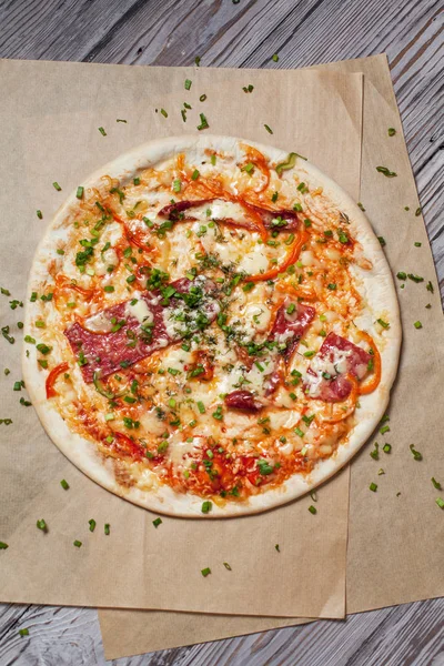 Pizza with a thin crust with cheese, bacon, pepper and herbs on a light wooden background
