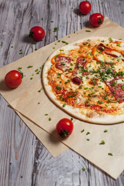 Pizza with a thin crust with cheese, bacon, pepper and herbs on a light wooden background