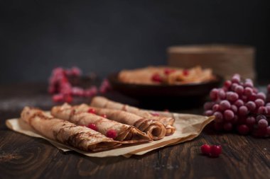 bir yığın ile tatlı taze kek ve krep pişirme kağıda haddelenmiş tübüllerin, kartopu meyveleri koyu gri arka plan üzerinde koyu ahşap bir masa üzerinde ile