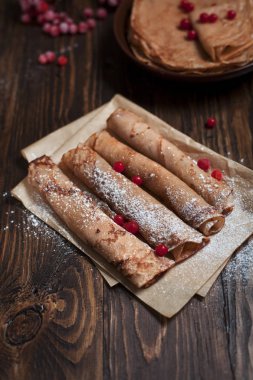 bir yığın ile tatlı taze kek ve krep pişirme kağıda haddelenmiş tübüllerin, kartopu meyveleri koyu gri arka plan üzerinde koyu ahşap bir masa üzerinde ile