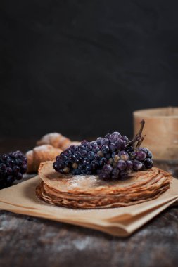 Fırından yeni çıkmış tatlı krep pişirme kağıdı, kruvasan ve üzüm koyu gri arka plan üzerinde koyu kahverengi ahşap masa üzerinde yığılmış