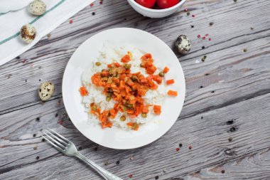 haşlanmış havuç, bezelye ve soğanlı beyaz tabakta, bıldırcın yumurtası ile lezzetli pirinç kase kiraz domates, biber ve açık gri renkli bir ışık ahşap masada havlu ile