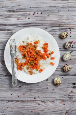haşlanmış havuç, bezelye ve soğanlı bir beyaz tabak, bıldırcın yumurtası, biber ve ahşap masa lambası çatalı ile lezzetli pirinç