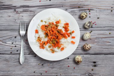 haşlanmış havuç, bezelye ve soğanlı bir beyaz tabak, bıldırcın yumurtası, biber ve ahşap masa lambası çatalı ile lezzetli pirinç