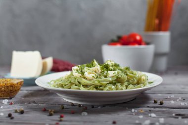 ham spagetti, peynir, dereotu ve kiraz domates hafif ahşap bir masa üzerinde bir kase ile tabak makarna ıspanak ve mozzarella peyniri ve beyaz bir plaka, Fransız hardalı, yeşillik ile yeşil renkli