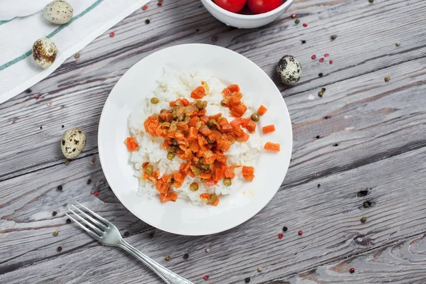 haşlanmış havuç, bezelye ve soğanlı beyaz tabakta, bıldırcın yumurtası ile lezzetli pirinç kase kiraz domates, biber ve açık gri renkli bir ışık ahşap masada havlu ile